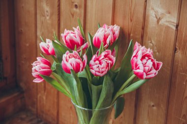 Pencerenin yanında vazoda laleler var. Pencerenin yanında ahşap bir masa üzerinde bir vazo içinde çiçek buketi.
