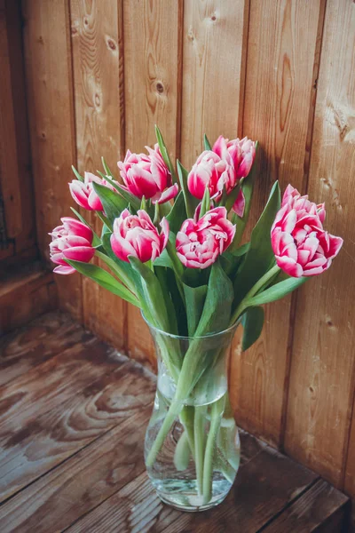 Tulips in a vase by the window. Bouquet of flowers in a vase on a wooden table by the window.