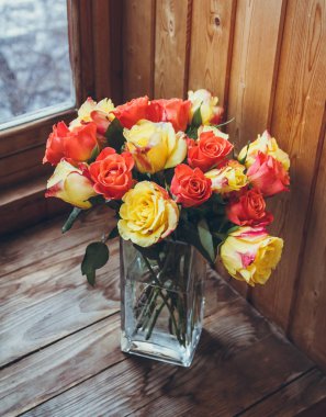 Ahşap bir arka plan üzerinde vazoda gül buketi. Vazoda çiçekler. Şeffaf vazo. Vazoda turuncu ve sarı çiçekler.