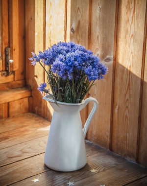 Beyaz demir sürahideki mısır çiçeğinin çiçekleri. Sürahi ahşap bir rafta duruyor. Bir sürahi çiçek bir buket.