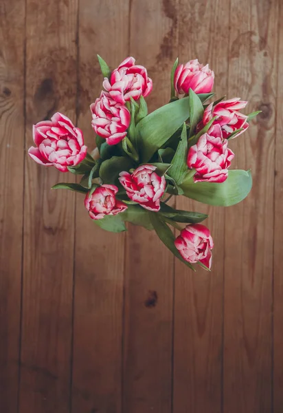 Tahta bir masada çiçek buketi. Vazoda laleler. Çiçek buketi üst görünümü.