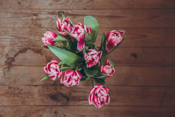 Tahta bir masada çiçek buketi. Vazoda laleler. Çiçek buketi üst görünümü.