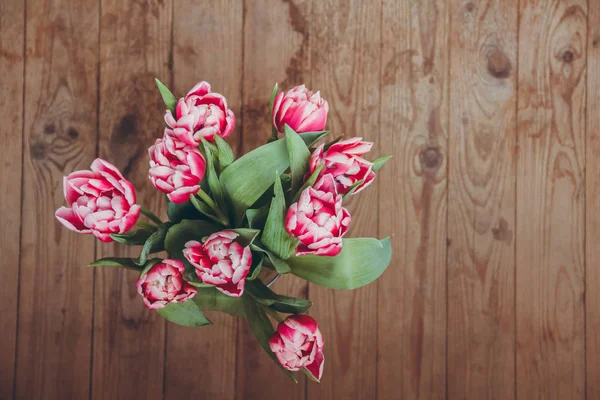 Tahta bir masada çiçek buketi. Vazoda laleler. Çiçek buketi üst görünümü.