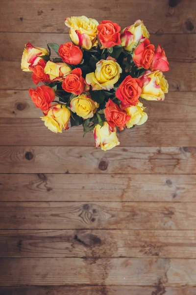 Bouquet of roses on a wooden background. View from above. Yellow and orange roses. Bouquet of flowers on the table.