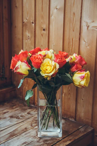 Ahşap bir arka plan üzerinde vazoda gül buketi. Vazoda çiçekler. Şeffaf vazo. Vazoda turuncu ve sarı çiçekler.