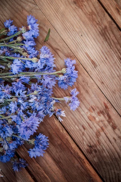 Na dřevěném stole leží květiny z kukuřičných květů. Pohled shora. Kytice modrých květů na dřevěném pozadí. — Stock fotografie