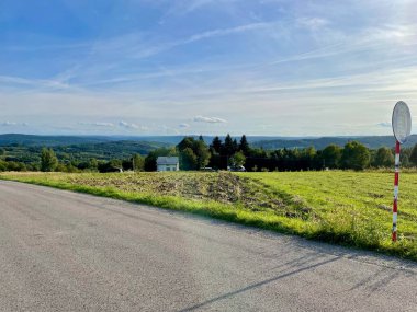 Yol kenarında duran bir tabela, arka planda dağ eteklerinin manzarası..