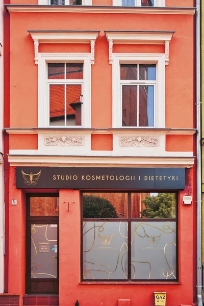 Üzerinde Stüdyo Cosmetologi i Dietetki yazan siyah tabelası olan bir bina. Bina turuncu ve bir sürü penceresi var.