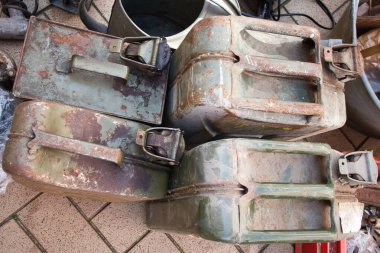 Paslı saplı dört eski metal konteynır tuğla zeminde duruyor. Konteynırlar farklı boyutlarda ve şekillerde, ama hepsinin görünüşü aynı. Sahne biraz kasvetli.