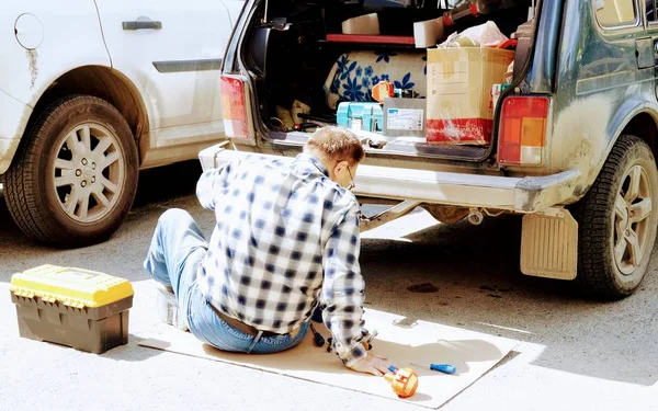Bir adam yerde oturan bir şeyi tamir eder..