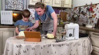 Önlüklü genç bir baba ve küçük oğlu mutfakta birlikte yemek pişiriyorlar. Aile tatillerini paylaşırlar, yemek hazırlama ve sıcak bir yuva ortamında eğlenceli etkileşimlerle eğlenirler.. 