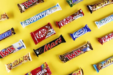 Kiev, Ukraine, March 29, 2018. different chocolate bars of modern companies. Chocolates lie in rows on a yellow background. Skittles - sweets, which are made by the company Vrigley. The rest of the chocolate is produced by Mars and Nestl clipart