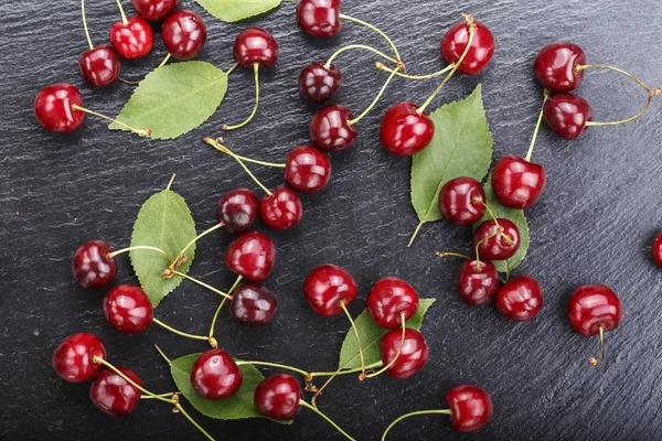 red sweet cherries and green leaves on a black slate backgroun