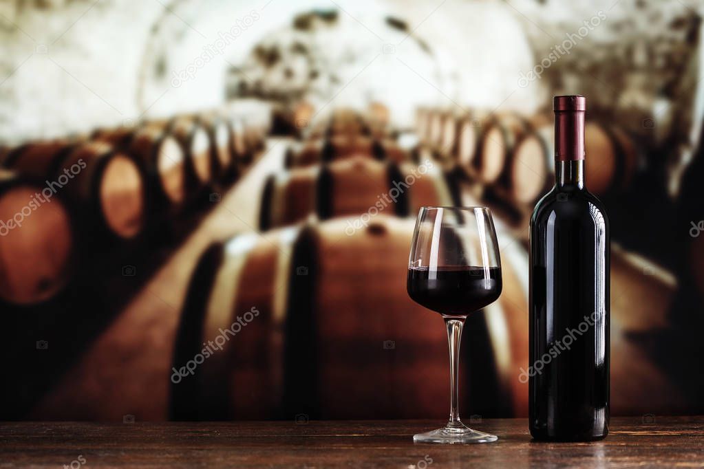 a glass and a bottle of wine on the background of barrels in the cella