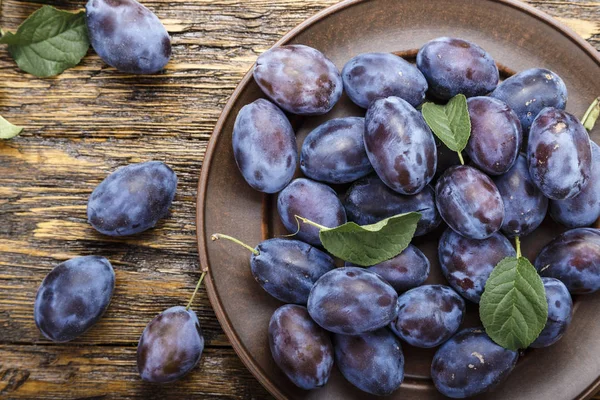 olgun erik bir tabak içinde ahşap bir zemin üzerine yeşil yaprakları ile. abov görüntülemek