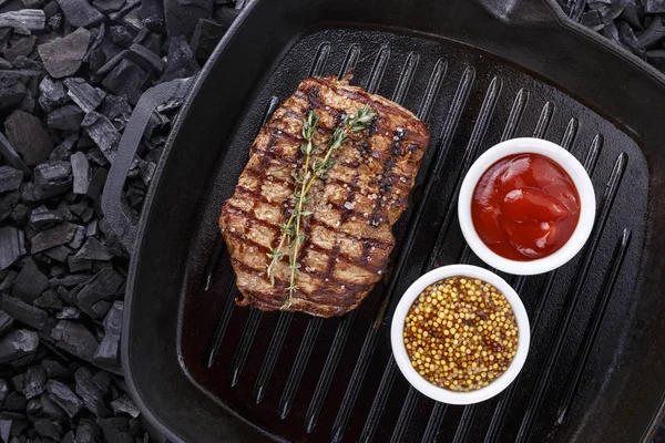 grilled steak on a black background. The steak lies on the grill pan. scattered spice