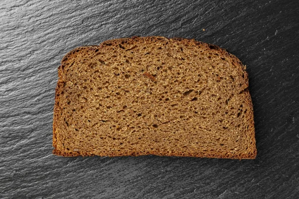 a slice of black bread on a black slate background. place for tex
