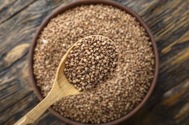 ahşap arka plan üzerinde bir kil plaka ham karabuğday kabuğu çıkarılmış tane. tahta kaşık plaka. tex için alan