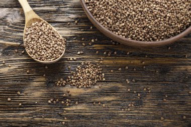 ahşap arka plan üzerinde bir kil plaka ham karabuğday kabuğu çıkarılmış tane. bir tahta kaşık yanındaki plakadır. tex için alan