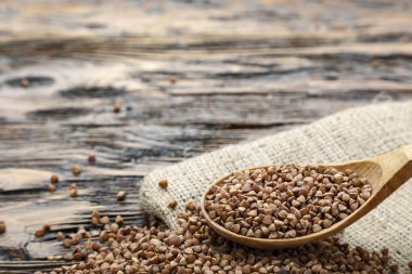 çuval bezi ahşap zemin üzerinde ham karabuğday kabuğu çıkarılmış tane. bir tahta kaşık. tex için alan