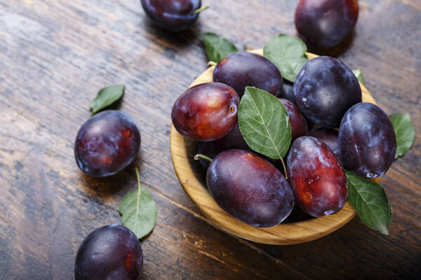 Спелые сливы в деревянной тарелке на темно-коричневом деревянном столе. деревенский стиль
