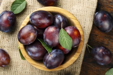 Olgun kırmızı erik bir plaka üzerinde eski püskü ahşap arka plan üzerinde bir çuval bezi. metin için yer