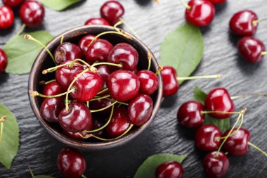 Olgun kırmızı kiraz yaprakları siyah bir arka plan ile bir kil tabak dağınık. tex için alan