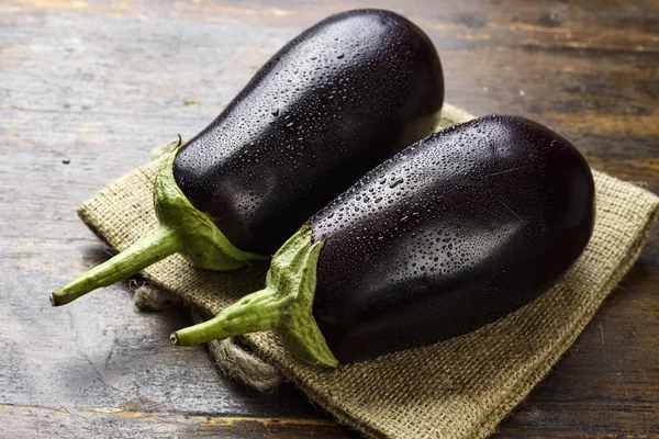 çuval bezi üzerinde yalan ahşap bir masa üzerinde iki Olgun patlıcan. tex için yer