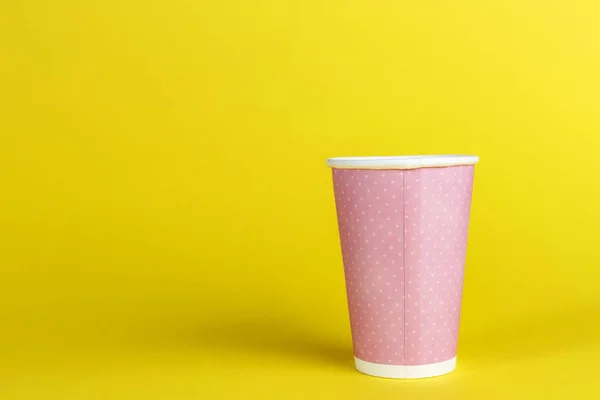 pink cardboard cup for coffee without a cap on a yellow backgroun