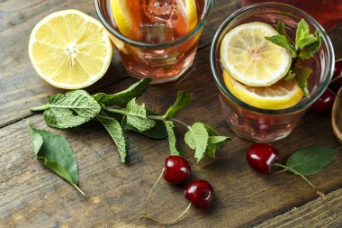 Ev yapımı tatlı kiraz kompostosu bir bardak limonlu ahşap arka plan üzerinde. Yakınlarda çilek ve yeşil bırakın bulunmaktadır