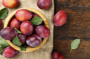 Olgun kırmızı erik bir plaka üzerinde eski püskü ahşap arka plan üzerinde bir çuval bezi. metin için yer
