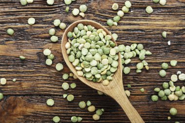 Kahverengi ahşap bir masa üzerinde bir kaşık çiğ kuru bezelye. tex için alan