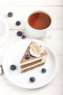 bir dilim kek krem katmanlar üzerinde bir daire ve bir cu çay ile taze yaban mersini ile