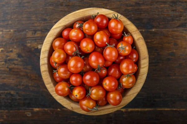 Red cherry tomatoes in a plate on a brown wooden table. space for tex