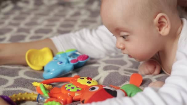 Barnet ligger på sängen med leksaker — Stockvideo