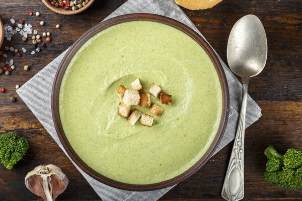 bowl of broccoli and green peas cream soup on wooden table 