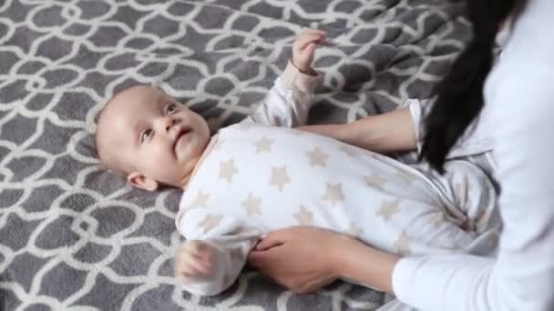 A mãe brinca com o bebé. bebê jaz na cama na parte de trás . — Vídeo de Stock