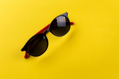 Kırmızı kollu, sarı arkaplanlı unisex güneş gözlükleri. metin için yer