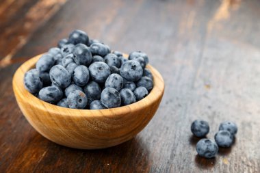 Tahta bir masada, ahşap kasede taze toplanmış yabanmersini. Sağlıklı meyve.