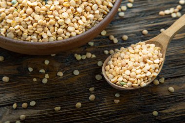 Kahverengi ahşap bir masada ve ahşap bir kaşıkta kuru sarı bezelyeler.