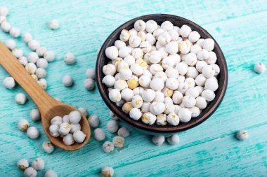 Çamurdan bir tabakta ahşap bir zeminde pişmemiş kuru beyaz nohutlar. Yakınlarda bir kaşık yatar.