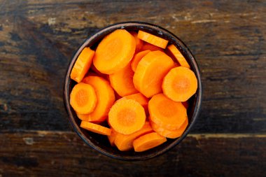 Kahverengi ahşap zemin üzerinde bir tabakta dilimlenmiş çiğ havuç. Yukarıdan görünüm