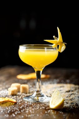 Sarı tropikal kokteyl, ahşap bir tezgahın üzerinde zarif bir bardakta. Çubuk şeker bardağın yanına serpilmiş. tex için yer