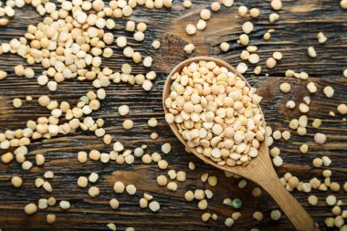 Kahverengi ahşap arka planda tahta kaşıkta kuru bezelyeler. tex için yer