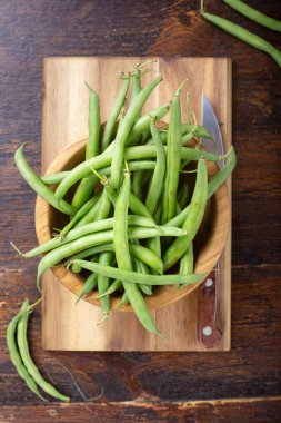 Kesme tahtasındaki çiğ taze kuşkonmaz fasulyesi, kahverengi ahşap sırtüstü