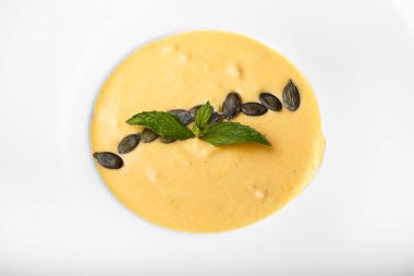 Beyaz tabakta balkabağı kremalı çorba. Çorbada fasulye kabağı ve fesleğen yaprakları var. en üstteki görünüm