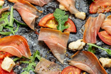 Pizza carbonara yakın çekim. Mozzarella, pastırma, zeytin, parmesan ve kırmızı soğanlı siyah pizza. İtalyan gelenekleri.