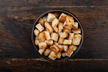 Ahşap arka planda bir kasede çıtır çıtır kızarmış ekmek. Üst görünüm.