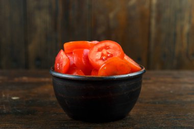 Ahşap arka planda bir kasede dilimlenmiş kırmızı domates. Sebze, malzeme ve zımba. Sağlıklı yemek..