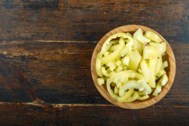 Ahşap arka planda bir kasede dilimlenmiş çiğ sarı biber. Sebze, malzeme ve zımba. Sağlıklı yemek..